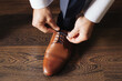 Brown leather shoe lacing. Businessman in white shirt and suit trousers. Groom getting ready for the wedding. Wearing clothes background. Dressing up male fashion. Business fashion hotel room.	
