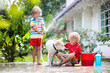 © famveldman - Kids wash dog in summer garden. Water hose fun.