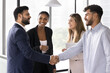 © fizkes - Happy confident diverse male business partners shaking hands at meeting, standing in office hall, closing deal, getting agreement, finishing successful work project with handshake
