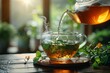 Green tea being poured from a clear teapot into a teacup with fresh leaves, showcasing health and natural wellness