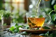 Hot tea being poured into a clear glass surrounded by fresh green leaves on a wooden surface