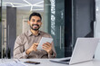 © Liubomir - A confident young businessman with a warm smile works on a tablet while sitting at a desk in a sleek, contemporary office environment. He displays professionalism and approachability.