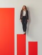 A professional woman stands on ascending red blocks against a white backdrop, symbolizing career growth and overcoming obstacles.