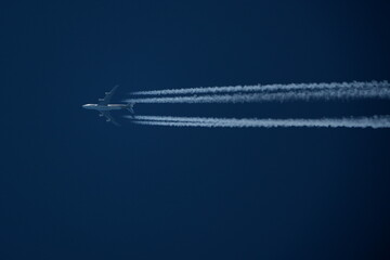 Wall Mural - Airplane in the blue sky with contrails in the air.