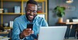 © grigoryepremyan - Busy African American guy, sits at his desk, using a mobile phone while working,
