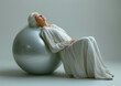 © AmayaGB - Mujer mayor 70s haciendo ejercicio de fuerza con las piernas ejerciendo presión con su espalda sobre la pelota de pilates plateada, relajación, musculatura, equilibrio, yoga
