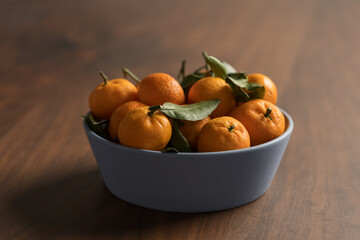 Wall Mural - Small organic tangerines with leaves in ceramic bowl on wood table