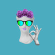 Antique female statue's head with roses on it, in sunglasses showing the ok gesture with hand isolated on a blue color background. Trendy collage in magazine style. 3d contemporary art. Modern design
