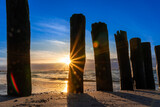 Fototapeta Dmuchawce - Beautiful golden hour beach sunset with glowing sun and colorful sky shows vibrant colors as north sea sand dunes and nature reserve at the ocean in golden hour sunshine as travel destination agents