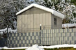 Graue Gartenhütte aus beschichtetem Stahlblech und Kunststoff sowie Metallgitterzaun mit Folienbespannung als Sichtschutz im Garten eines ländlichen Einfamilienhaus im Winter