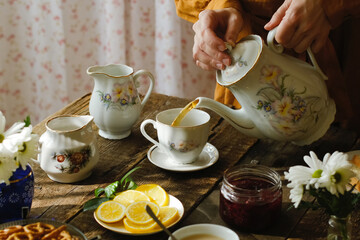 Wall Mural - Tea party in rustic style. Pouring tea from teapot into porcelain cup.