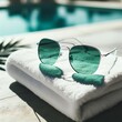 Sunglasses and towel by the poolside, basking in the sunlight. Featuring green shades and polarized lenses, the sunglasses reflect vivid colors