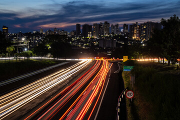 Wall Mural - Trail of light caused by vehicular traffic in SP-294, Comandante Joao Ribeiro Barros Highway with buildings from downtown in the background, in Marília,