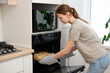 The girl puts the pizza in the oven. A young woman preparing cheese pizza in the kitchen