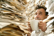 © innluga - funny portrait of a insurance broker looking at a tall pile of papers while holding the coffee cup in his hands