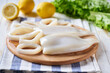 Squid whole and cut into rings, lemon, garlic, parsley on a wooden table.