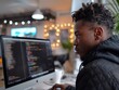 © MaxK - A man is sitting in front of a computer monitor, typing on a keyboard. He is wearing a black hoodie and has a beard. The room is dimly lit, and there is a potted plant in the background
