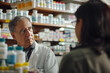 © punniix - A focused male pharmacist in a white coat gives advice for a woman in a pharmacy with medicines in the background
