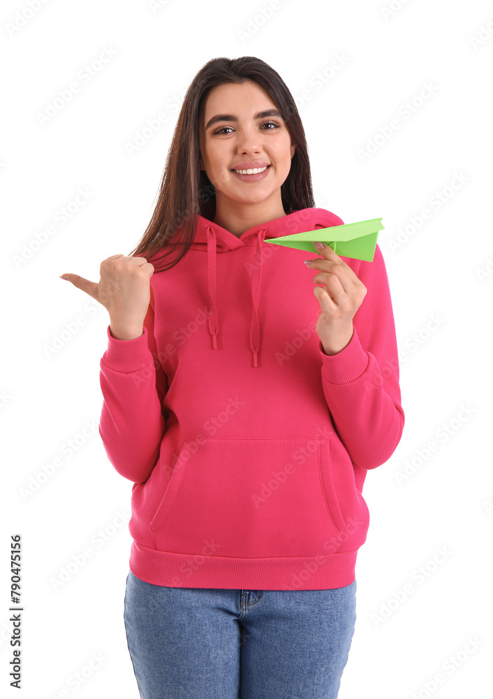 Young woman with paper plane pointing at something on white background