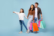 © Home-stock - Seasonal sales. Family holding colorful paper shopper bags, girl pointing aside at free space, standing on blue background