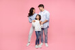 © Home-stock - European parents embracing their happy daughter looking at pretty girl, standing together on pink studio background, full length shot