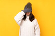 © luismolinero - Young woman with winter hat over isolated yellow background covering eyes by hands. Do not want to see something
