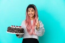 Young Woman With Pink Hair Holding Birthday Cake Isolated On Blue Background Showing And Lifting A Finger