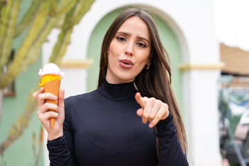 Wall Mural - Young pretty woman with a cornet ice cream at outdoors surprised and pointing front