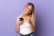 © luismolinero - Young blonde woman using mobile phone isolated on purple background points finger at you