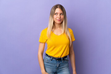 Wall Mural - Young blonde woman isolated on purple background having doubts while looking side