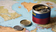 A jar filled with cash, displaying the Liechtenstein flag, sits atop a map. Saving for vacation, leisure activities. Financial planning, travel budget allocation