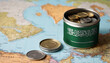 A jar filled with cash, displaying the Saudi Arabia flag, sits atop a map. Saving for vacation, leisure activities. Financial planning, travel budget allocation