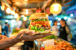 Street food. Male hand presents gourmet street burger, its layers of fresh lettuce, tomato, cheese, and a succulent patty showcased against the vibrant blur of bustling food street market
