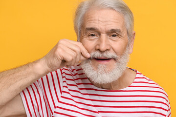 Wall Mural - Senior man touching mustache on orange background