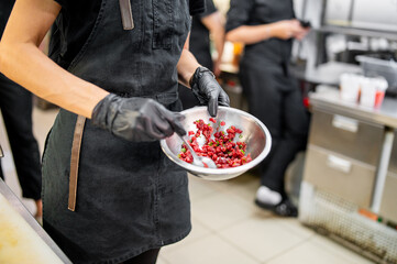 Wall Mural - Professional chef in a kitchen, wearing black apron and gloves, holding a bowl of fresh red meat, emphasizing meticulous preparation and quality