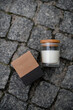 Soy-scented candle in a glass jar and a cardboard box from it lie on the pavement paved