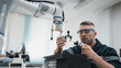 © NewSaetiew - Engineering student assembling a robotic arm using a computer in a technology workshop. Service engineer holding a robot controller and inspecting the robotic arm's welding hardware.