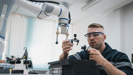 Engineering student assembling a robotic arm using a computer in a technology workshop. Service engineer holding a robot controller and inspecting the robotic arm's welding hardware.