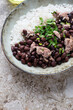 Black beans with chicken meat and white rice, vertical shot on a light-brown granite background, middle closeup