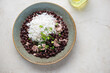 Rustic plate with cuban-style black beans and white rice, horizontal shot on a light-beige stone background, above view, copy space