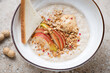 Oatmeal porridge served with peanut butter, fresh apple slices and granola in a white bowl, horizontal shot, middle close-up