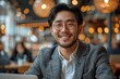 Happy Asian man with glasses using a laptop in a café setting