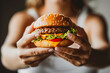 womans hands holding a nice big tasty hamburger or burger with grilled beef and salad, unhealthy fat fast or junk food