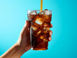 A hand holding a cup of ice cold soda with a straw in it