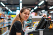 © pilipphoto - Portrait of a young smiling woman working as cashier at supermarket