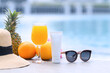 Free space bottle mock up products. Vitamin C skincare with fresh orange juice, hat, pineapples, and sunglasses near the swimming pool. travel vacation accessory.