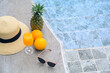 Time to relax on a summer day. Summer mood. Leisure at the pool. Fresh orange juice, hat, pineapples, and sunglasses near the swimming pool.