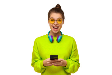 Wall Mural - Young teenage girl in green neon top and eyeglasses, wearing blue wireless headphones around neck, holding smartphone in hands and feeling excited and shocked