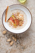 Bowl of oatmeal with peanut butter and fresh apple slices, above view on a beige granite background, vertical shot with space