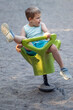 Little boy on a swinging rocking chair with one leg raised in a sand playground